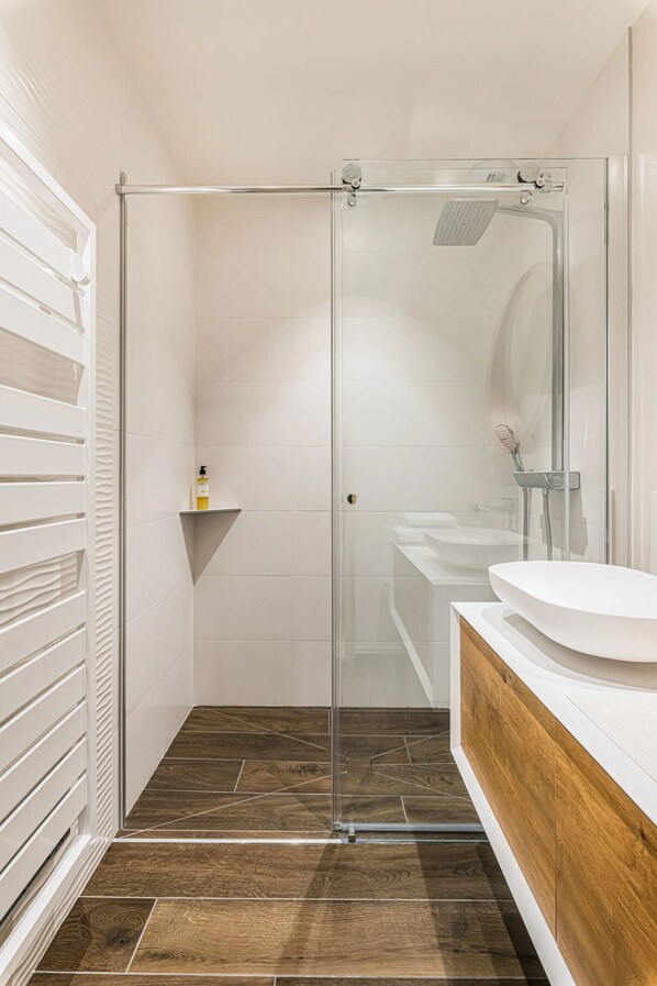 Un baño moderno con ducha de vidrio, tocador de madera y lavamanos blanco.