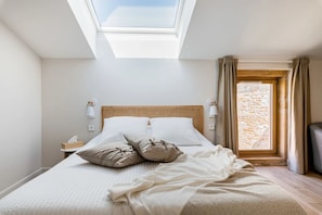 Un dormitorio con tragaluz, una cama con almohadas, lámparas de noche y vistas a una pared de piedra a través de una ventana.