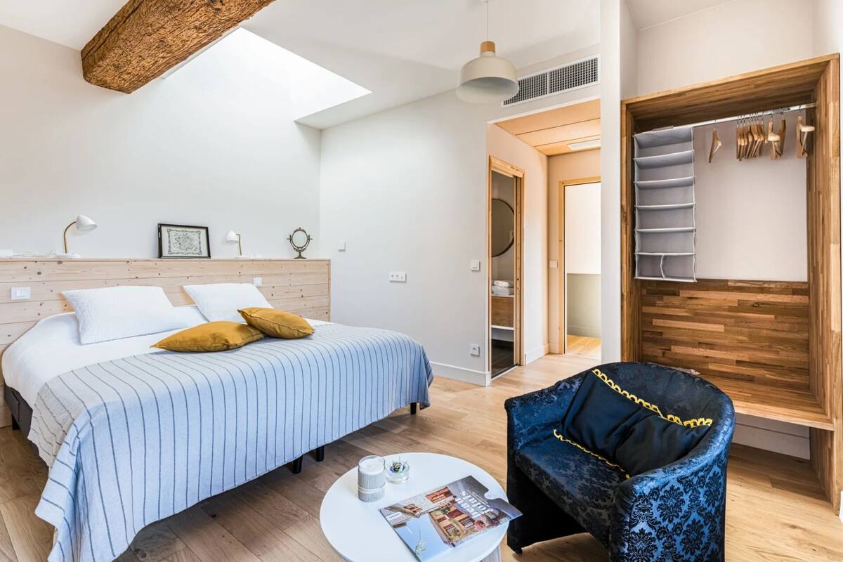 A bedroom with a bed, bedside table, and a chair. There is a wardrobe with hanging space and a mirror.
