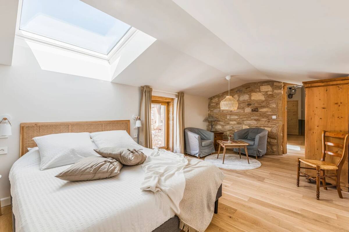 A bedroom with a skylight, a stone wall, and a cozy seating area.
