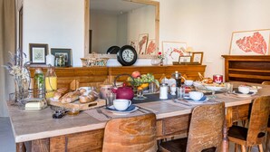 Een eetgedeelte met een houten tafel gedekt voor het ontbijt, inclusief brood, fruit en drankjes.