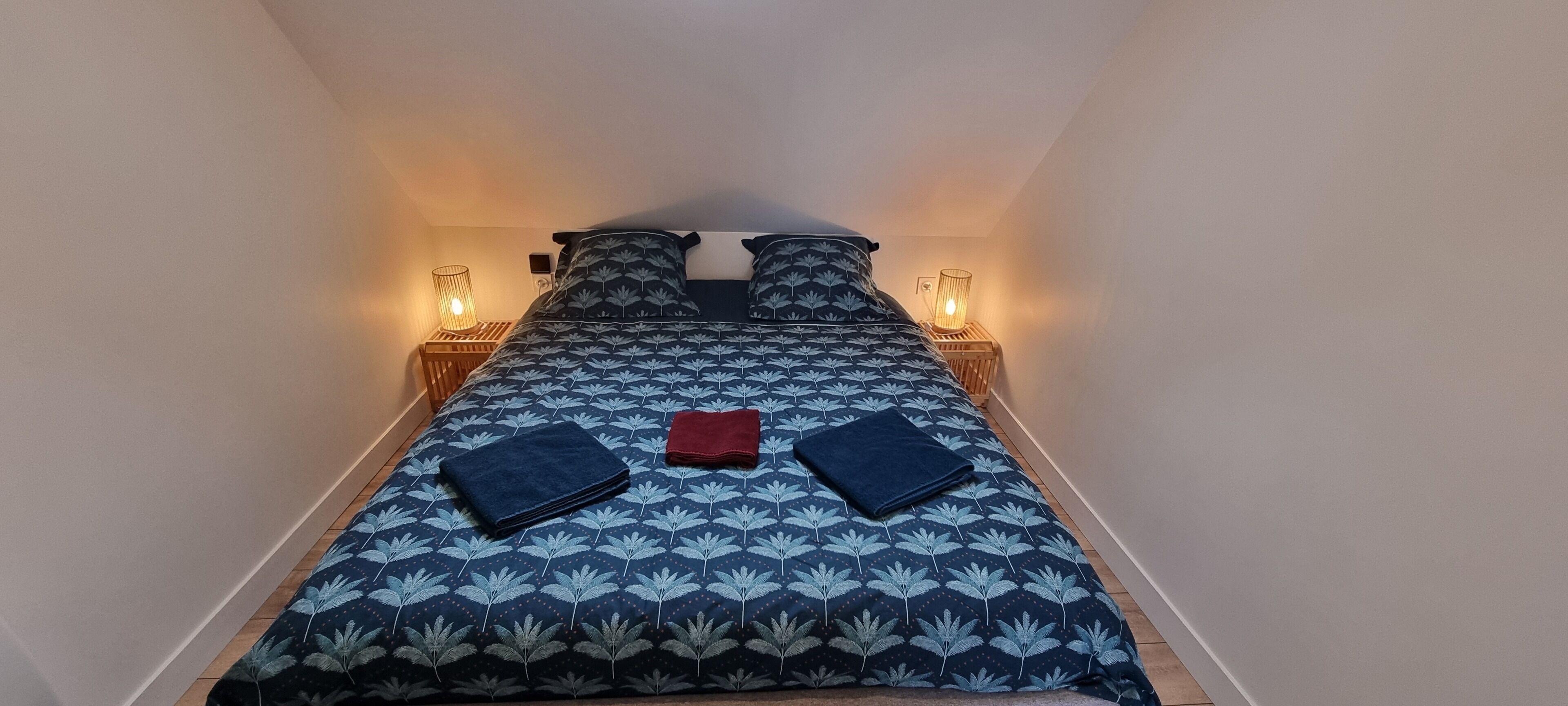 Een kleine kamer met een bed, twee bedlampen en een klein tafeltje.