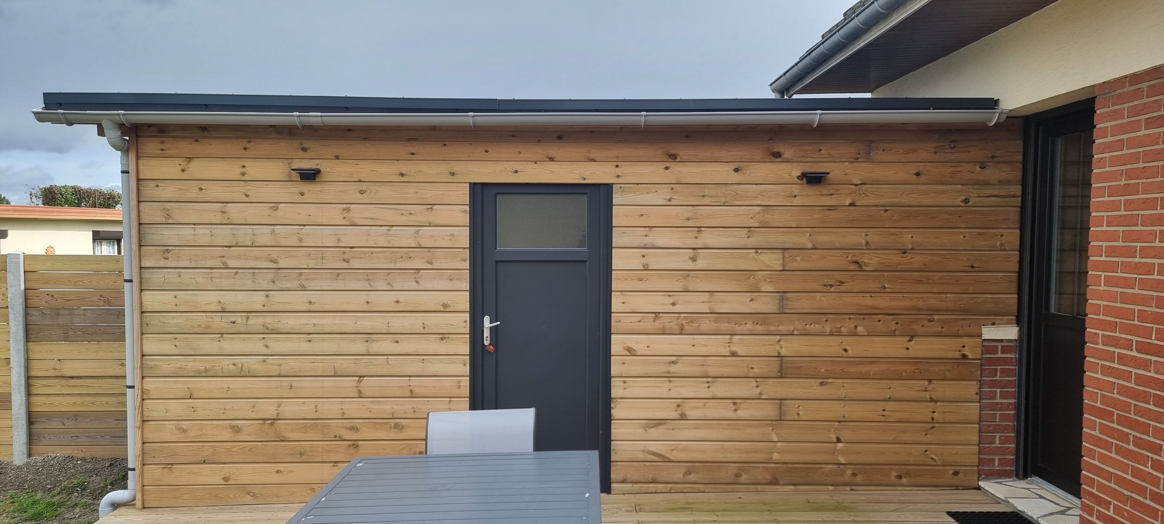 A wooden exterior with a black door and a small table in front.