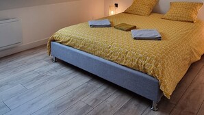 Un dormitorio con tragaluz, cama con ropa de cama amarilla y suelo de madera.