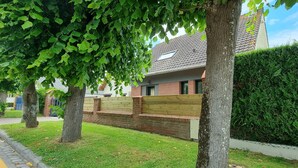 Un barrio residencial con una casa de fachada de ladrillo, cercada por una valla de madera y con un césped bien cuidado.