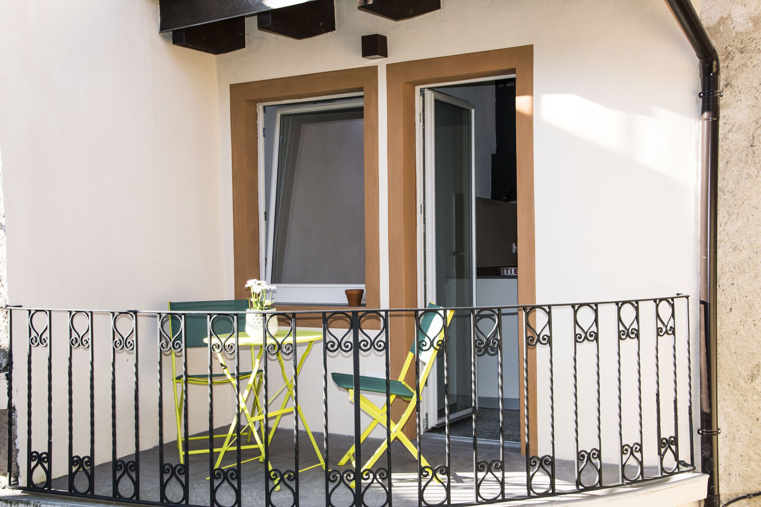 Ein Balkon mit schmiedeeisernem Geländer, einem gelben Stuhl und einem Tisch.