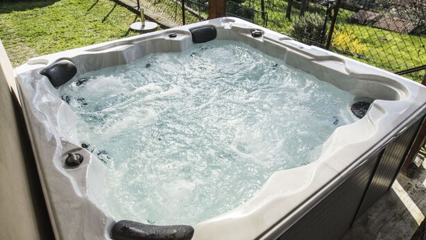 A hot tub with a clear view of the surrounding area, including a fence and a parked car.