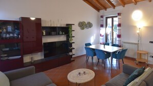 A living room with a TV, sofa, and dining area with chairs and a table.