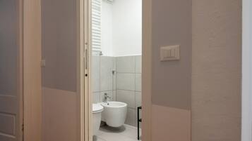 Ein Badezimmer mit Toilette, Bidet und einem schwarzen Metallstuhl.