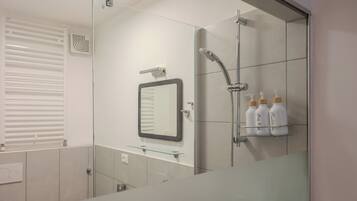 A modern bathroom with a glass shower enclosure, a wall-mounted mirror, and a shelf with toiletries.