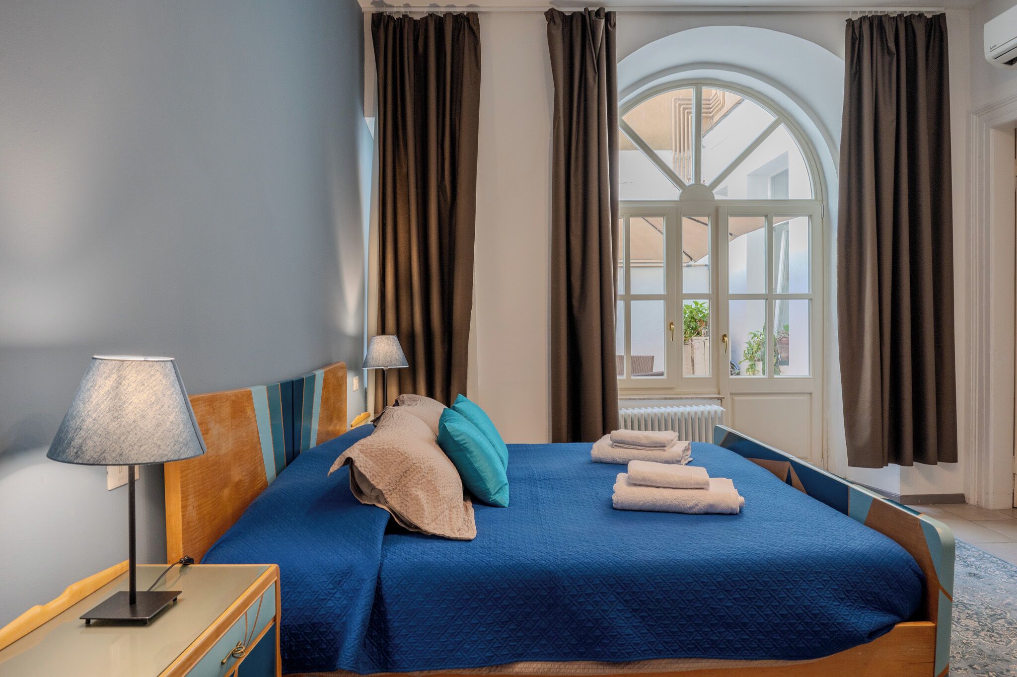 Une chambre d’hôtel avec un grand lit, une table de chevet avec une lampe, une vue sur l’extérieur par une fenêtre et un radiateur.