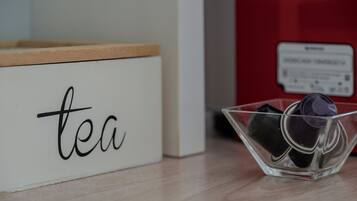 Eine weiße Box mit dem Wort 'tea', eine transparente Glasschale mit Teebeuteln und ein roter Behälter im Hintergrund.