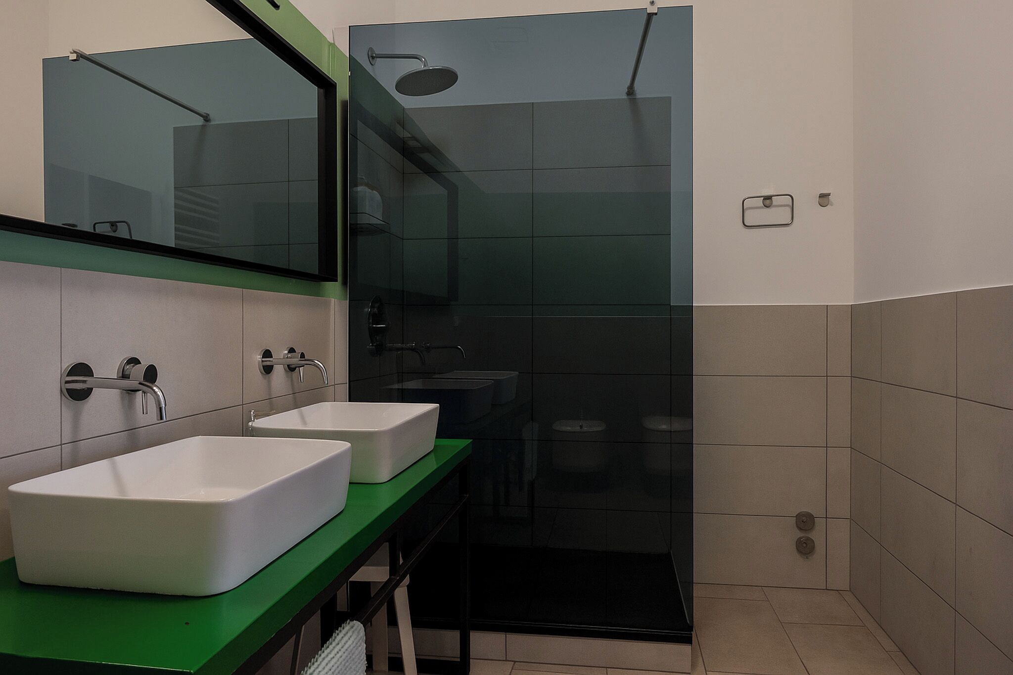 Une salle de bain moderne avec deux vasques blanches, un plan de toilette vert, un grand miroir et une douche séparée par une paroi de verre.