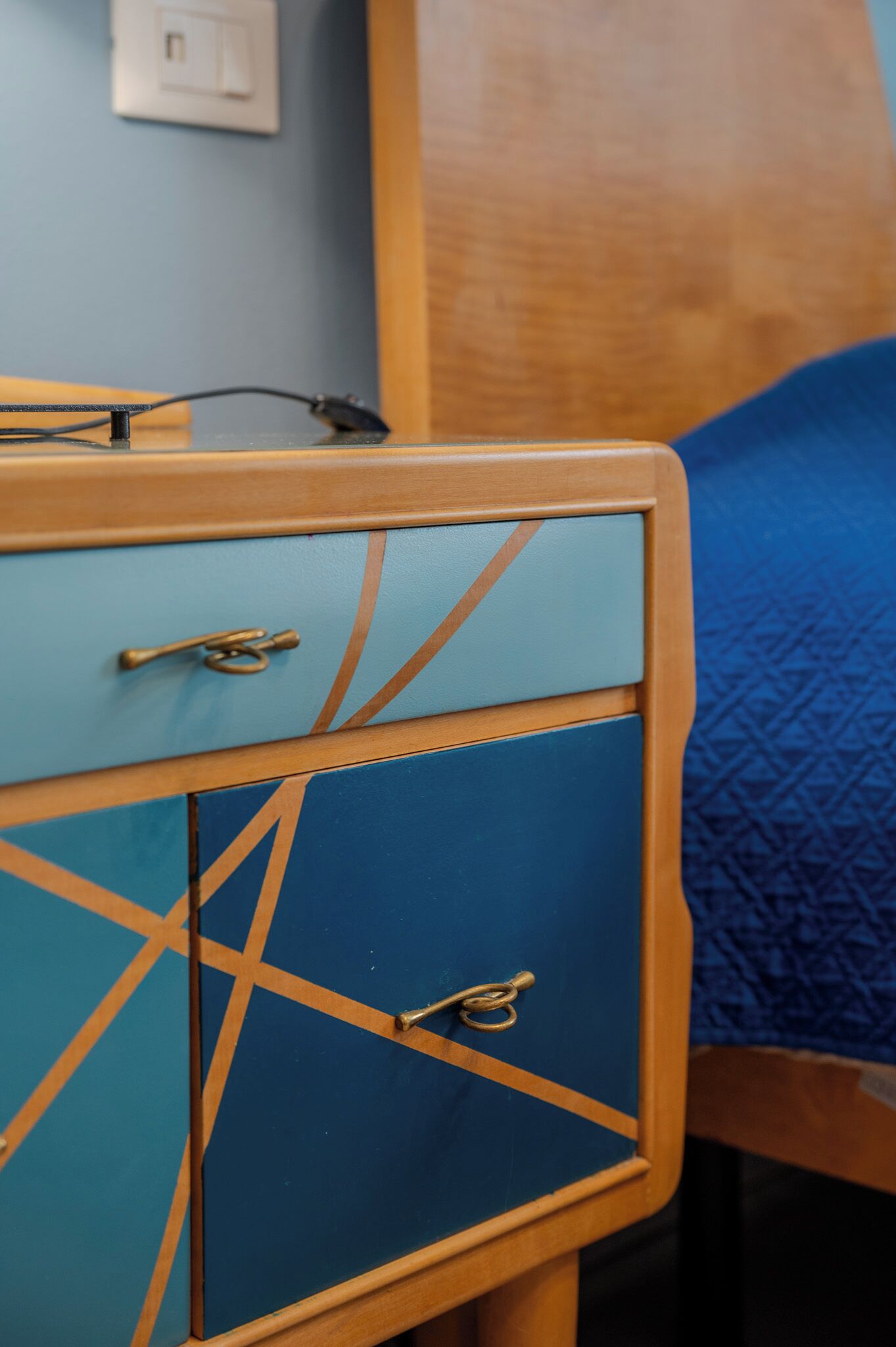A wooden bedside table with a blue drawer and a small cabinet.