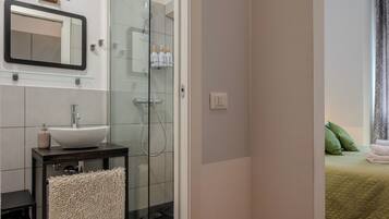 Ein Badezimmer mit einer Duschkabine aus Glas, einem Waschbecken mit Spiegel darüber und einem Handtuch auf einem Haken.