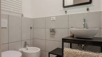 A modern bathroom with a white sink, bidet, and toilet.