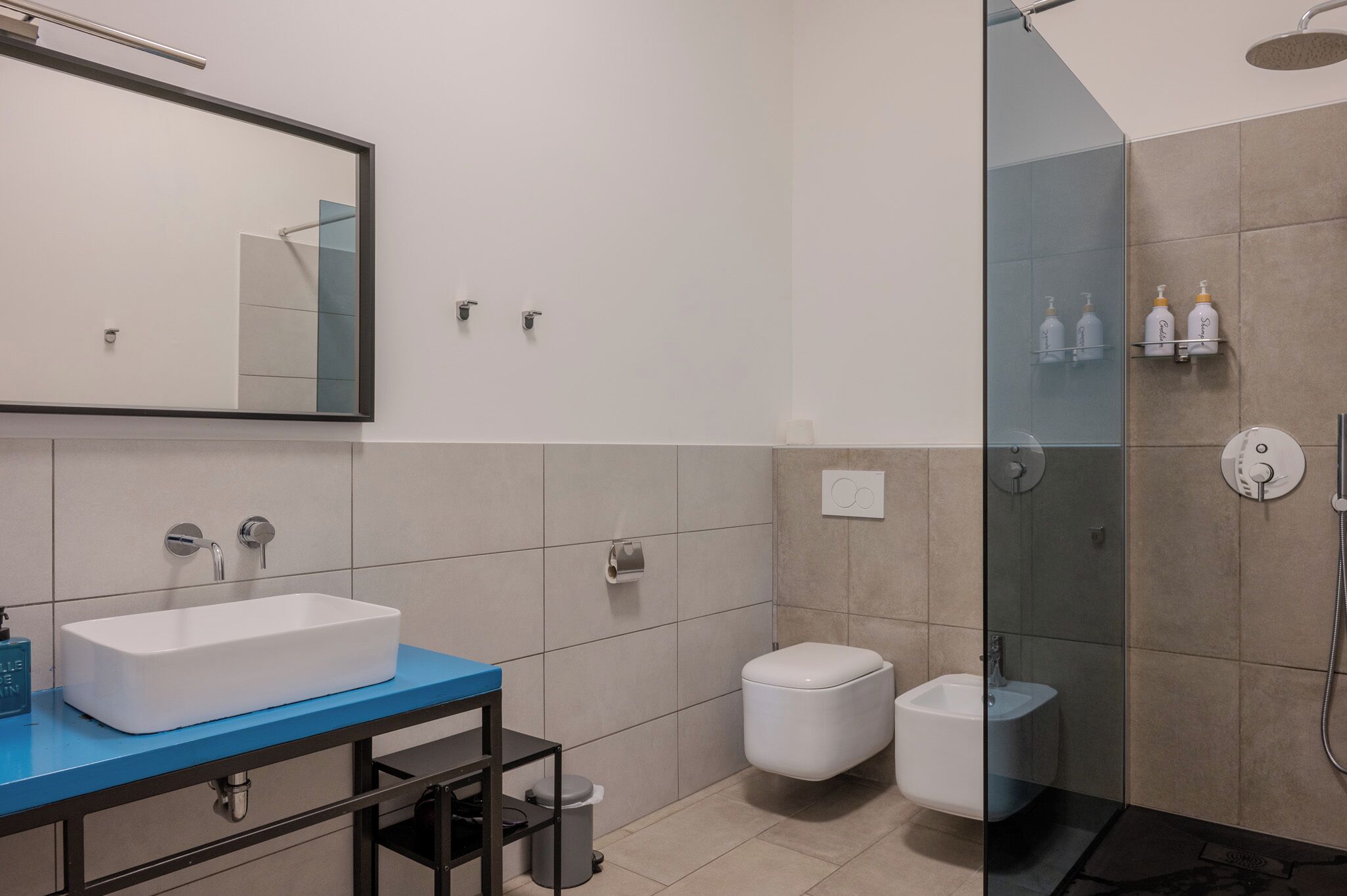Un baño moderno con un espejo grande, un lavabo blanco, un bidé y una zona de ducha con cerramiento de vidrio.
