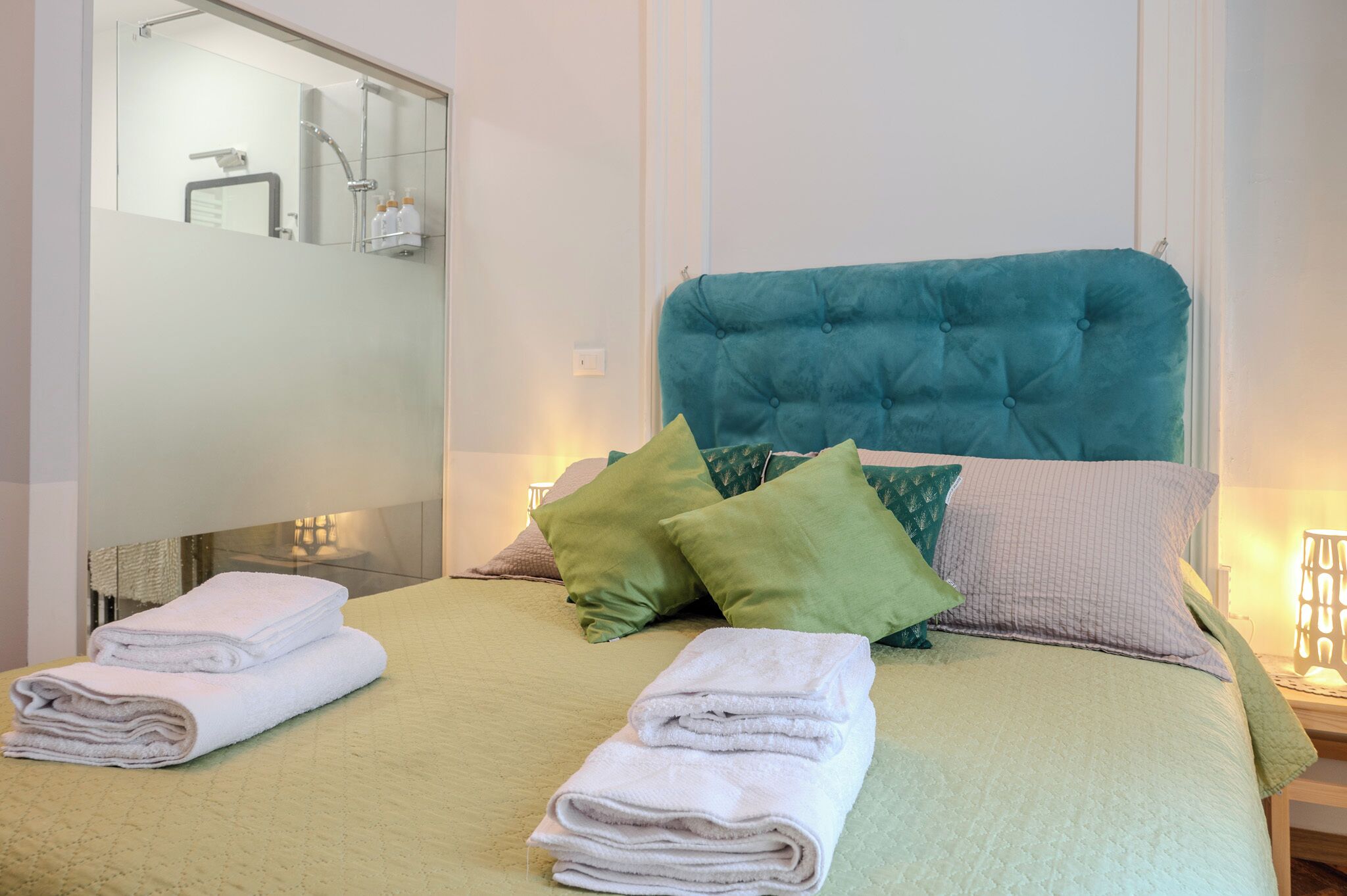 Una cama bien hecha con toallas dobladas, un cabecero capitonado y varias almohadas.