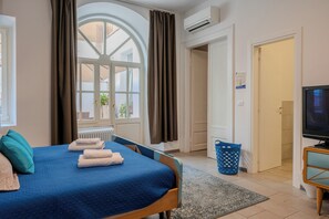 A hotel room with a bed, a TV, a radiator, a window with curtains, and a door leading to another room. - DA NOI A TRIESTE (Trieste)