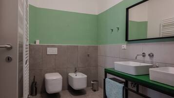 A bathroom with a green accent wall, a white toilet, a bidet, a sink with a mirror, and a towel rack.