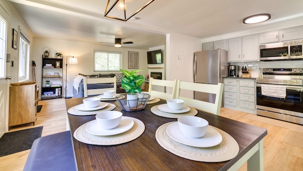 Una cocina moderna con armarios blancos, electrodomésticos de acero inoxidable y un comedor con mesa de madera para cuatro.