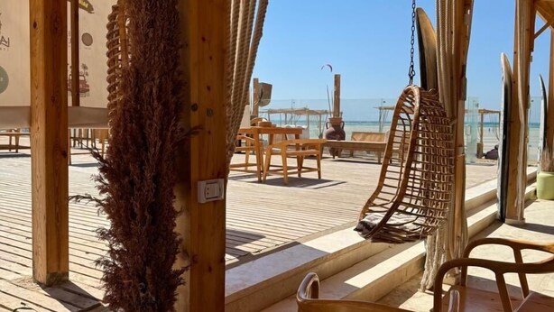 Un espace de détente en bord de mer, aménagé en bois, avec un fauteuil suspendu, un fauteuil rembourré et une table.
