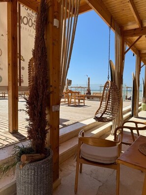 A wooden beachside seating area with a hanging chair, a cushioned chair, and a table. - La hacienda Modern and cozy (Ras Sudr)