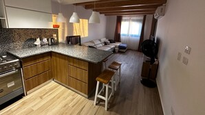 Une cuisine compacte dotée d’un comptoir en granit, de meubles en bois et d’une cuisinière encastrée. On y trouve également un coin salon avec un canapé et une petite table.