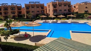 Une piscine entourée de chaises longues et de parasols, elle-même bordée d’un jardin aménagé et d’un bâtiment au style architectural traditionnel.