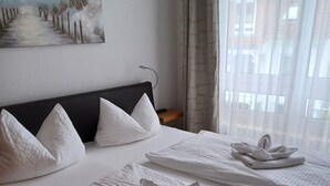 Et hotelværelse med en seng, hvidt sengetøj, puder og håndklæder pænt foldet.