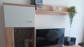 En moderne stue med et fladskærms-tv, en træhylde med et skilt, der står 'Mor', og en plante.