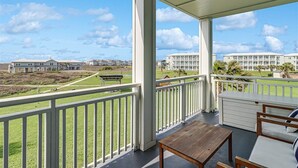 Un balcon abrité, doté d’une table et de chaises en bois, qui offre une vue sur une zone verdoyante et sur des bâtiments situés au loin.