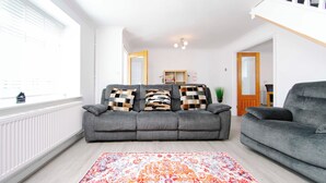 A living room with a grey sofa, patterned cushions, a colorful rug, and a white radiator. - Erin's Cottage in Merthyr Tydfil (Merthyr Tydfil)