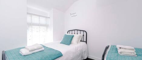 A bedroom with two beds, each with a teal patterned bedspread and white linens, a window with blinds, and a wall with a motivational quote.