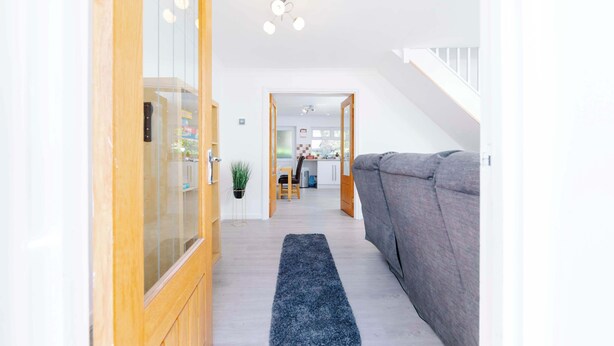 A hallway with a grey sofa, wooden cabinets, and a blue rug leading to a kitchen area. - Erin's Cottage in Merthyr Tydfil (Merthyr Tydfil)