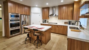 A modern kitchen with wooden cabinets, stainless steel appliances, a central island with stools, and a built-in sink. - 3 Bedroom, 4 bed/3 Bath, Close to Mountains, Downtown and Airport (Midvale)