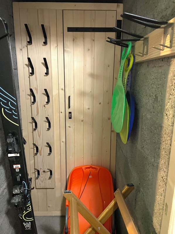 Une pièce avec un plancher en bois, une valise, un porte-manteau et un panier vert.