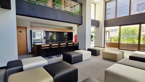 A modern lobby with a bar area, seating, and large windows offering views of the outside. - COBAR0131 - Edifício Único Barra (Salvador)