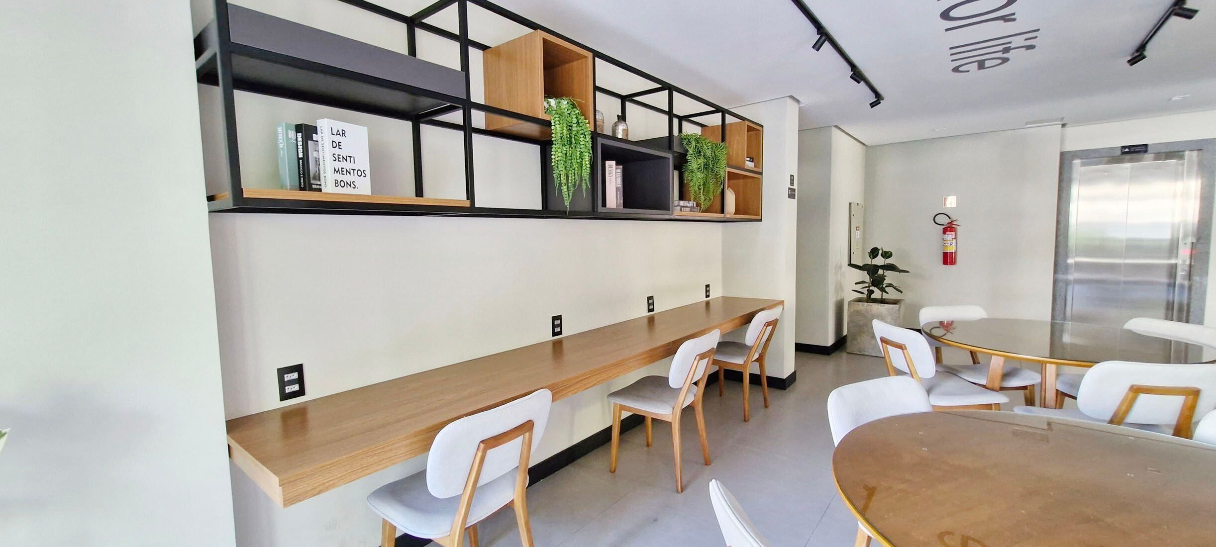 Una sala de reuniones moderna con una larga mesa de madera, sillas blancas y estanterías empotradas con plantas y libros.