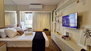 A hotel room with a bed, a TV, a desk, and a window with curtains. - COBAR0131 - Edifício Único Barra (Salvador)