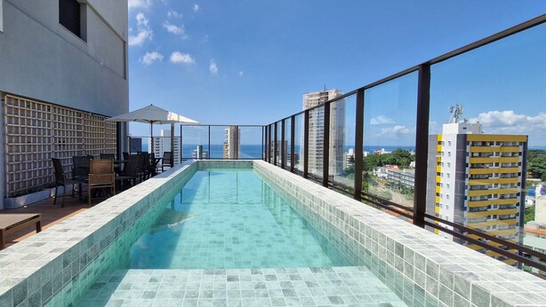 A rooftop infinity pool with a clear view of the ocean and surrounding buildings. - COBAR0131 - Edifício Único Barra (Salvador)