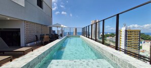 A rooftop infinity pool with a clear view of the ocean and surrounding buildings. - COBAR0131 - Edifício Único Barra (Salvador)