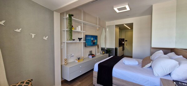 A modern hotel room with a bed, a TV, a desk, and a wardrobe. - COBAR0131 - Edifício Único Barra (Salvador)