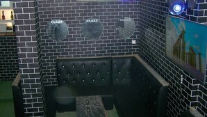 Une pièce aux murs recouverts de carreaux noirs, avec trois miroirs ronds, un banc noir rembourré et une petite table.