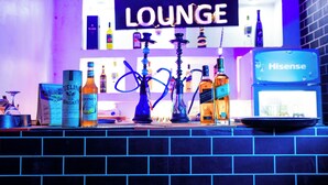 Un espace bar agrémenté d’un panneau indiquant « SALON », de diverses bouteilles et de narguilés.