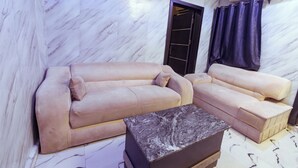 Un salon avec un mur aux motifs de marbre, un canapé beige, un fauteuil assorti et une table basse en marbre.