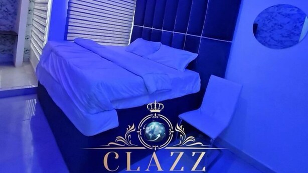 Une chambre à coucher moderne, baignée d’une lumière bleue, avec un lit recouvert de draps blancs et un motif décoratif sur la couvre-lit.