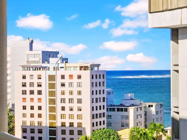 A coastal cityscape with modern buildings, including a prominent white building with multiple windows and balconies, and a view of the ocean. - Sand & Sun: Isla Verde Studio Near Beach & Airport (Carolina)