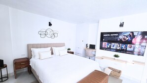 Une chambre à coucher moderne avec un grand lit, un téléviseur fixé au mur, une table de chevet et une petite plante.