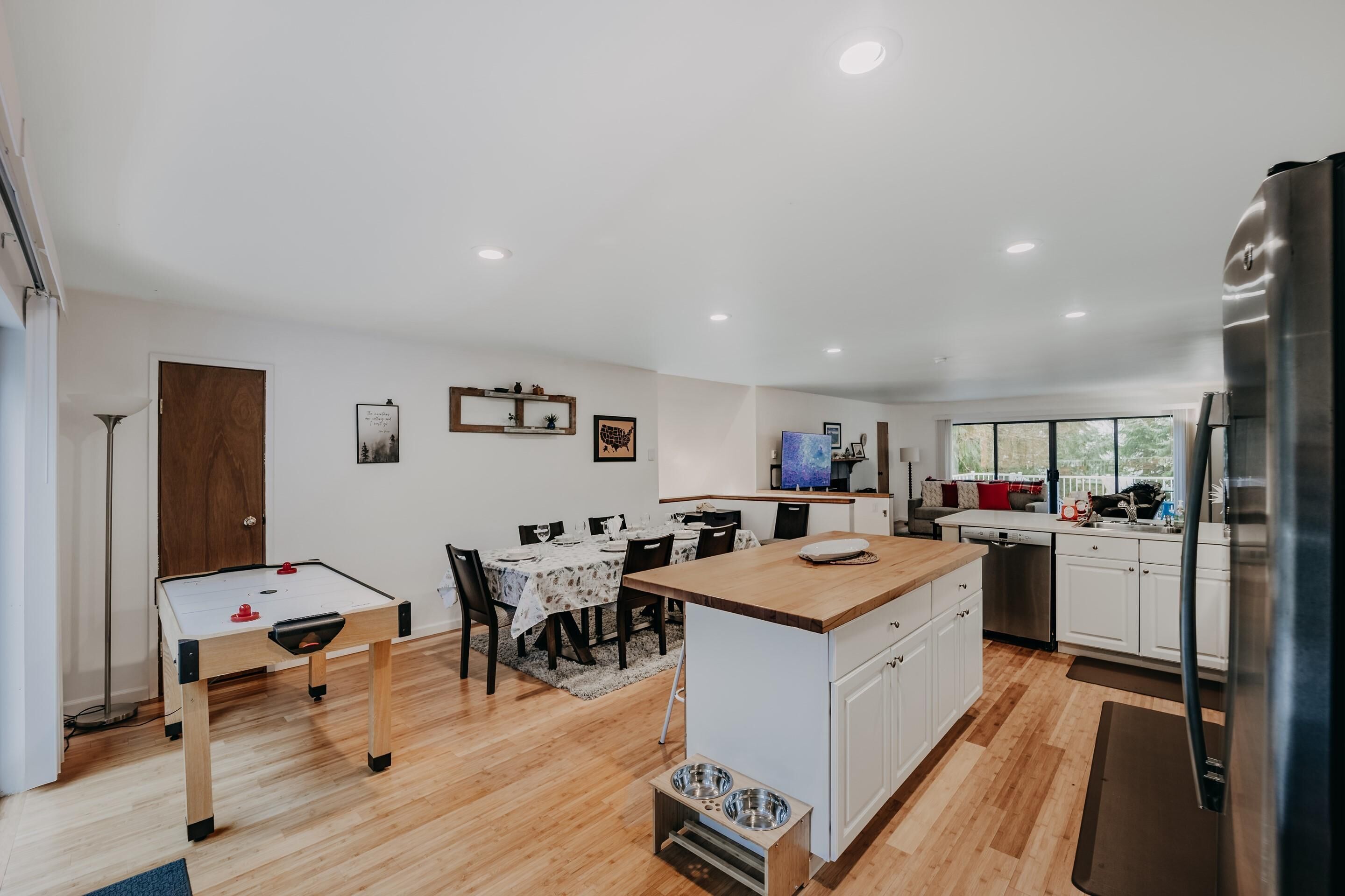 A modern kitchen with a central island, wooden flooring, white cabinetry, and a built-in dishwasher.